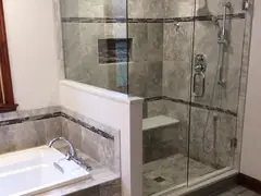 Frameless glass shower enclosure with stone tile beside a soaking tub