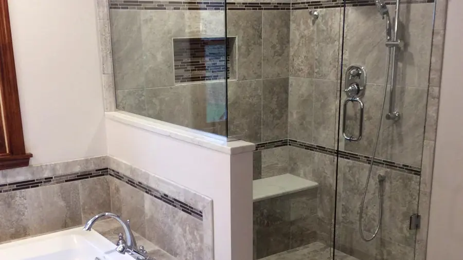 Frameless glass shower enclosure with stone tile beside a soaking tub